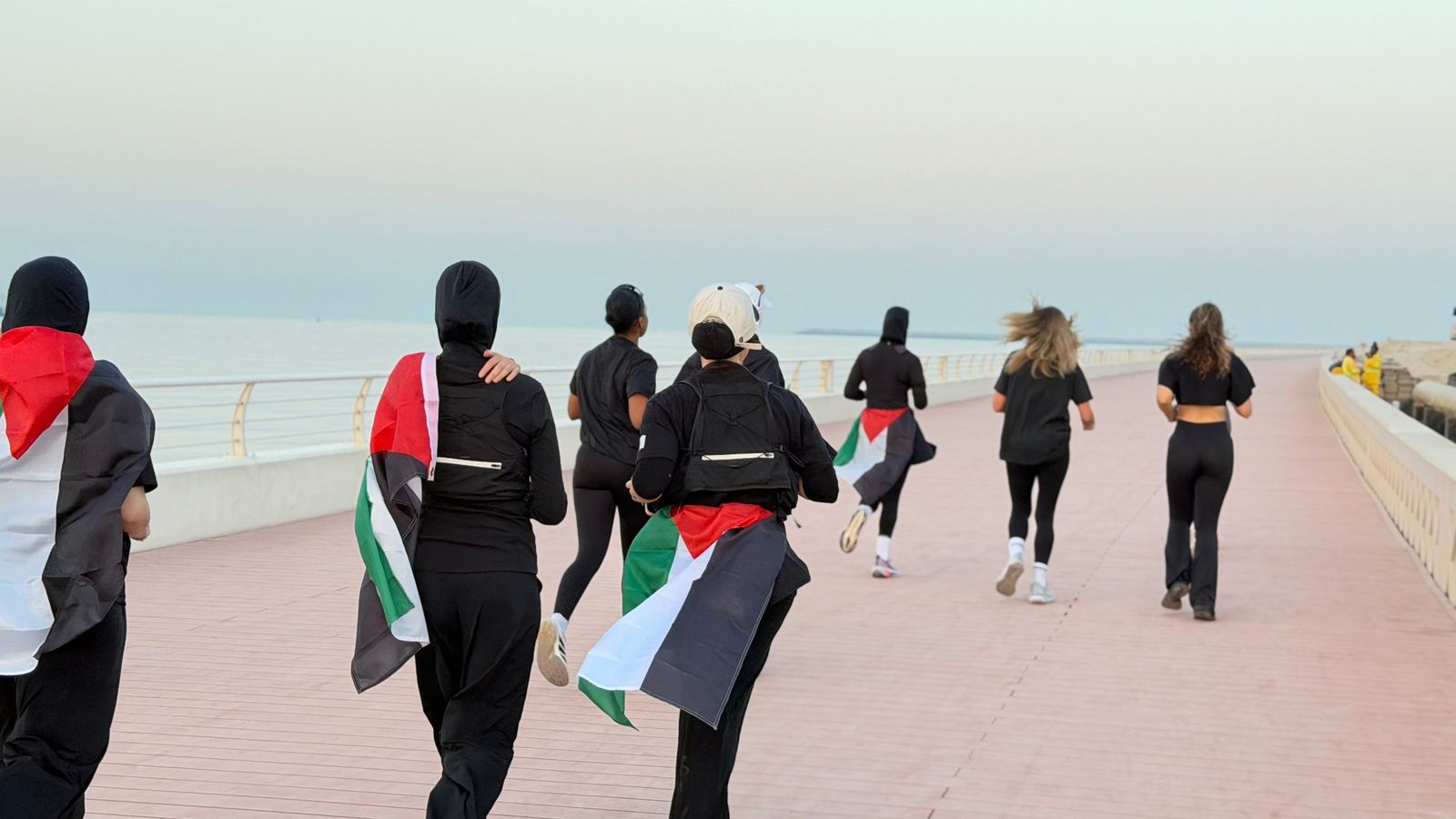 Runners carrying Palestinian flags along the waterfront